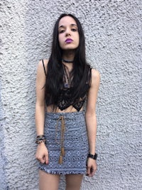 a young woman in a patterned skirt leaning against a wall